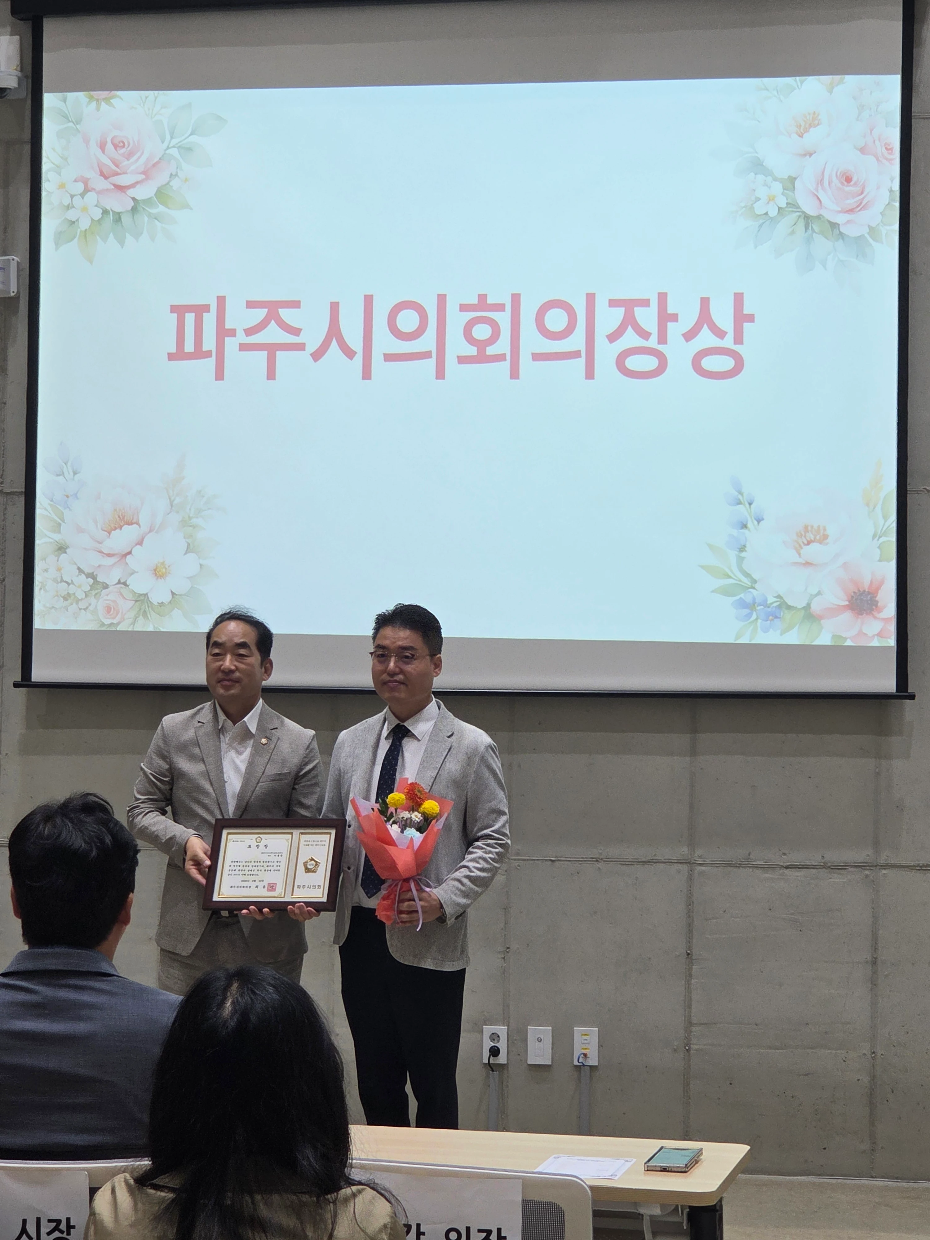 ‘파주시의회의장상’ 문구가 표시된 행사 화면 아래에서 이봉준 창업자가 꽃다발을 들고 시상자와 함께 표창패를 든 채 서 있으며 앞쪽에 참석자들이 보인다.